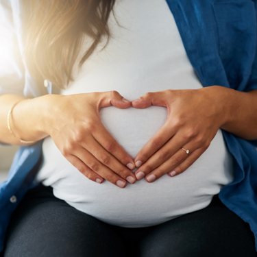 Der Bauch einer Schwangeren wird von Händen umfasst.